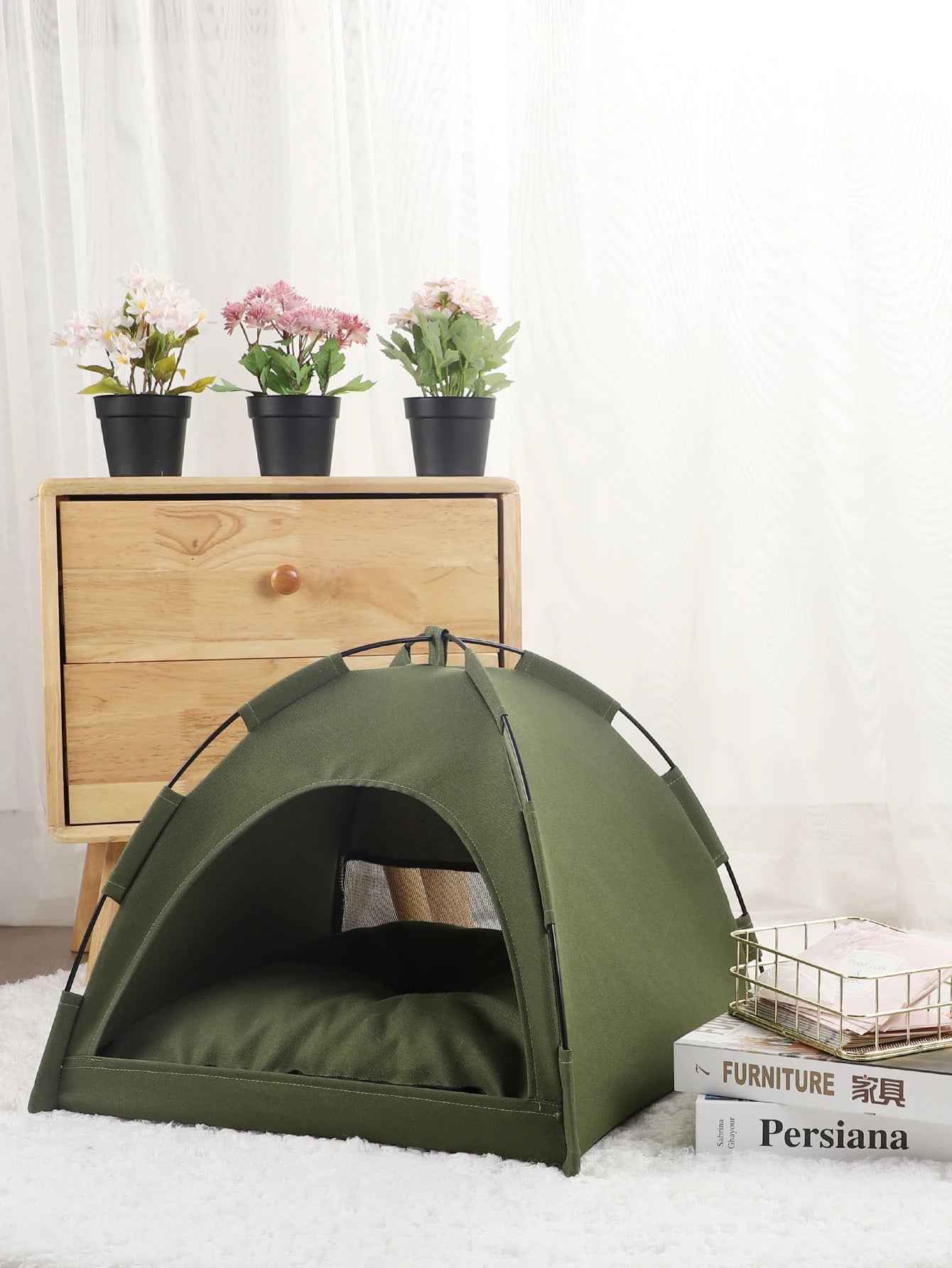 small olive drab green tent on a white carpet in front of a wooden dresser next to a stack of books