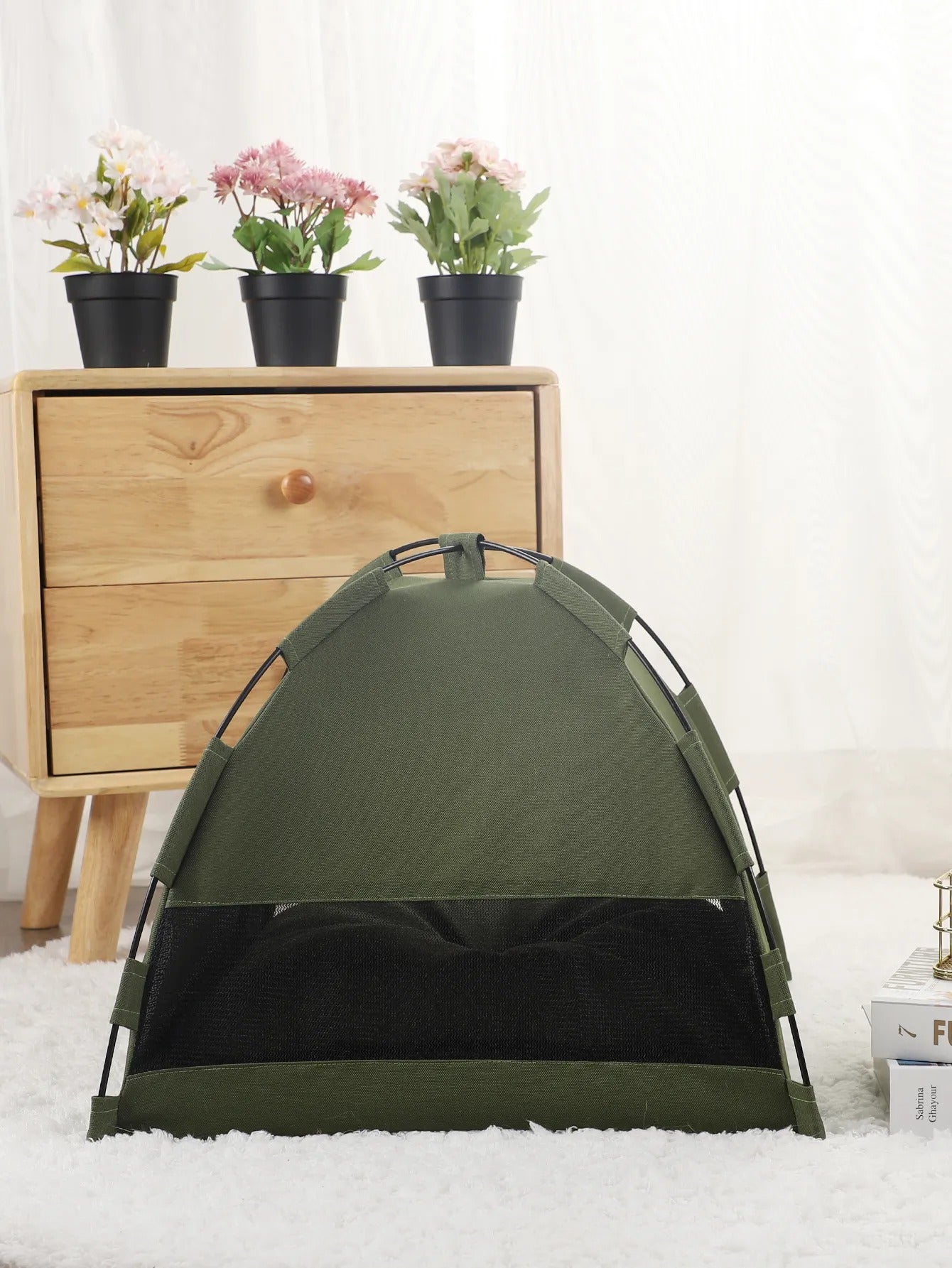 small olive drab green tent on a white carpet in front of a wooden dresser next to a stack of books