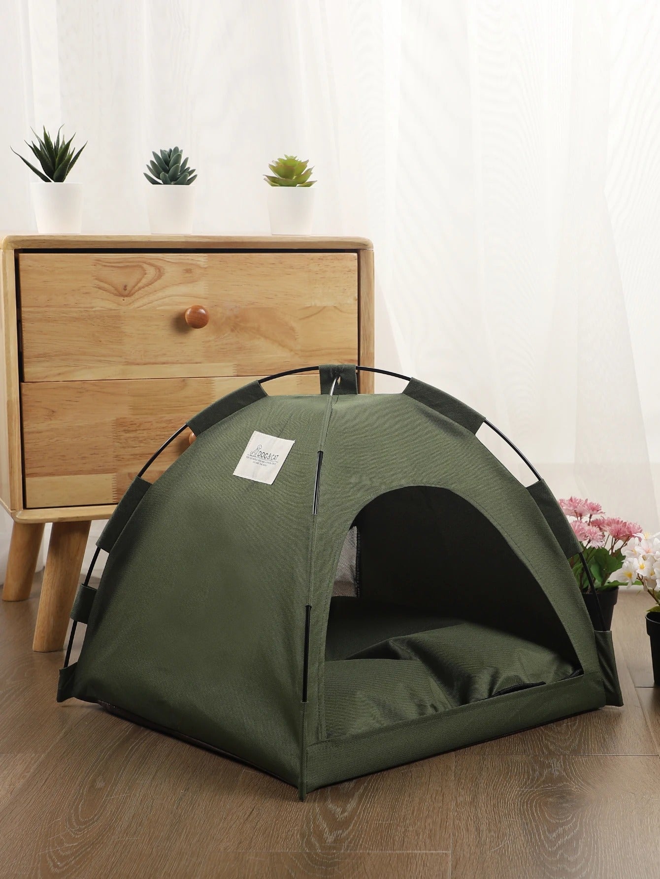 small olive drab green tent on hardwood floor in front of wooden dresser next to flower pots