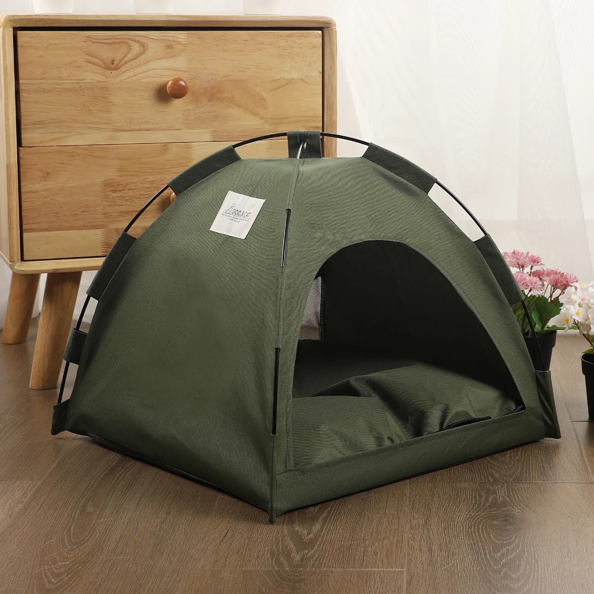 small olive drab green tent on hardwood floor in front of wooden dresser next to flower pots