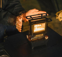 woman sitting outside warming her hands next to a vintage black kerosene oil lamp with brass knobs