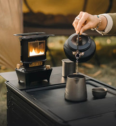 vintage black oil lamp outside on a table next to a woman pouring water from a kettle 